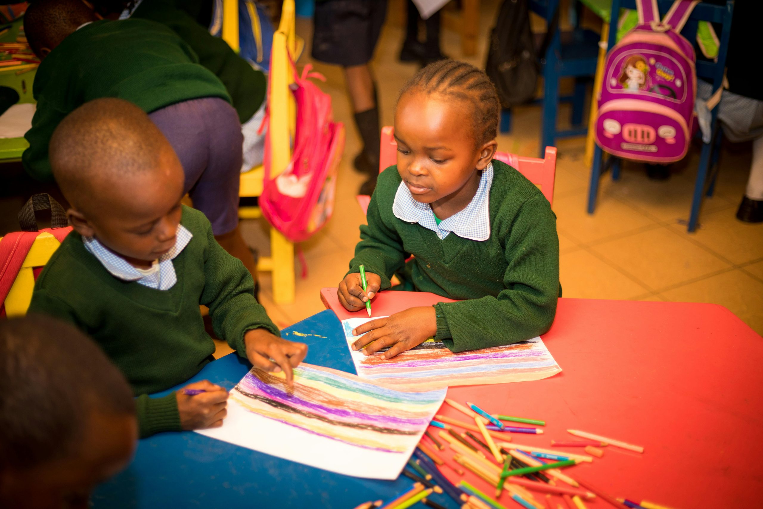 Two children enjoy coloring with pencils in a lively classroom setting.
